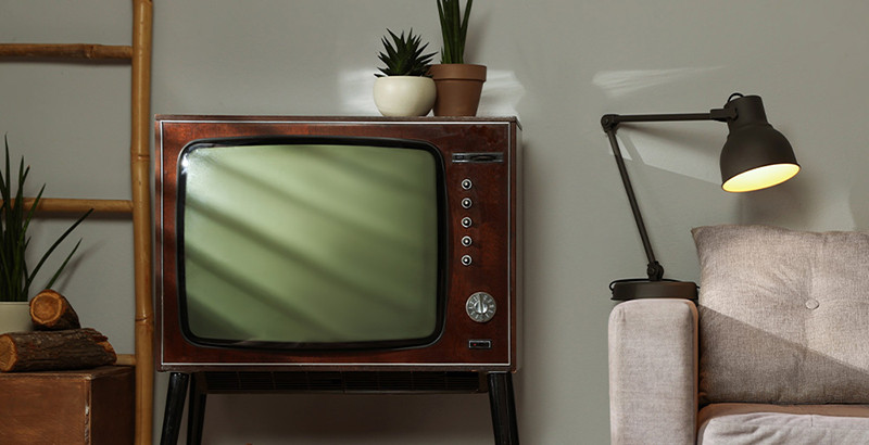 Retro televízor s obrúskom, zdobným kvetináčom a hodinami.